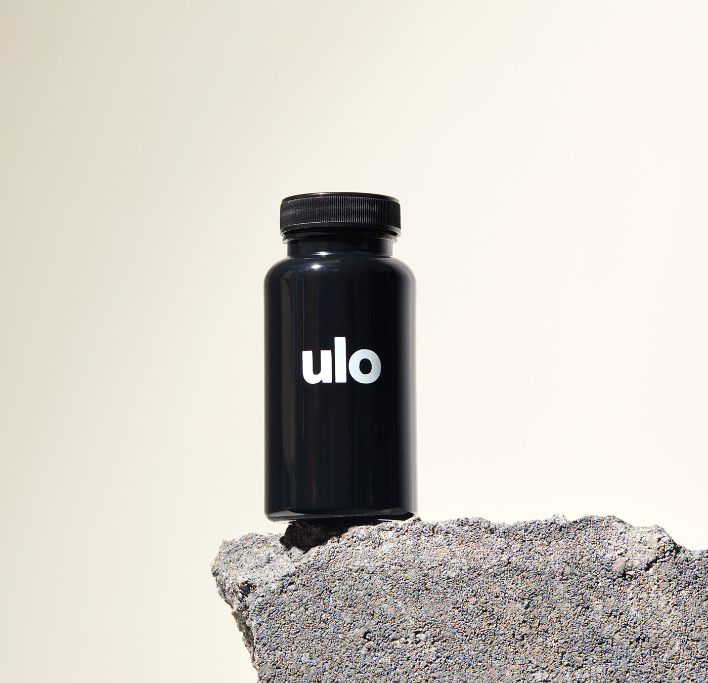 Oral minoxidil bottle placed on a gray rock with a beige background